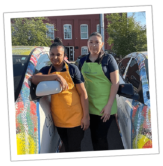 an image of two women employees of carpe diem between 2 cars of the company carpe diem, smiling